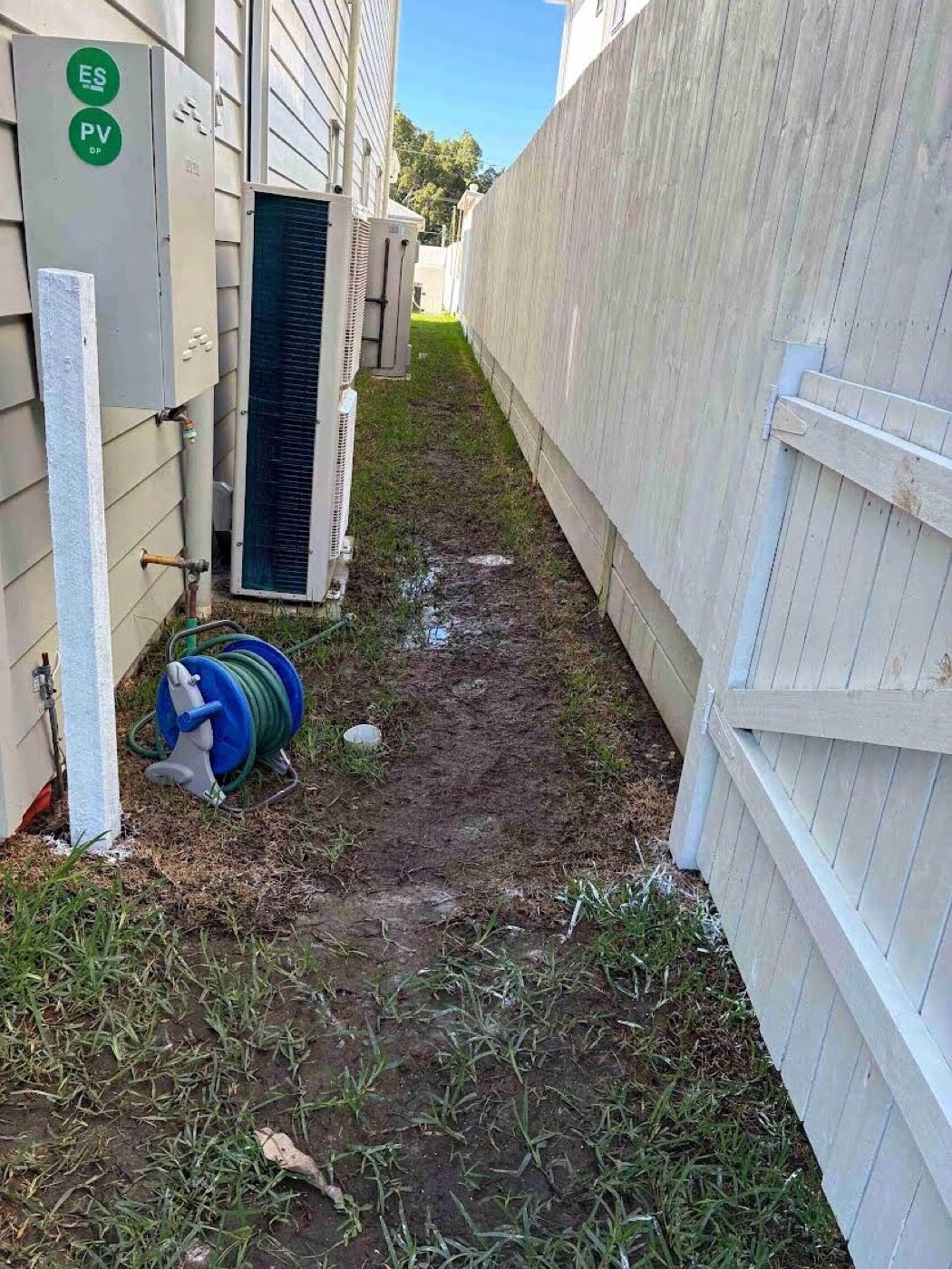 Exposed stormwater pipe in the muddy side path of a new-build home in Corinda, before work